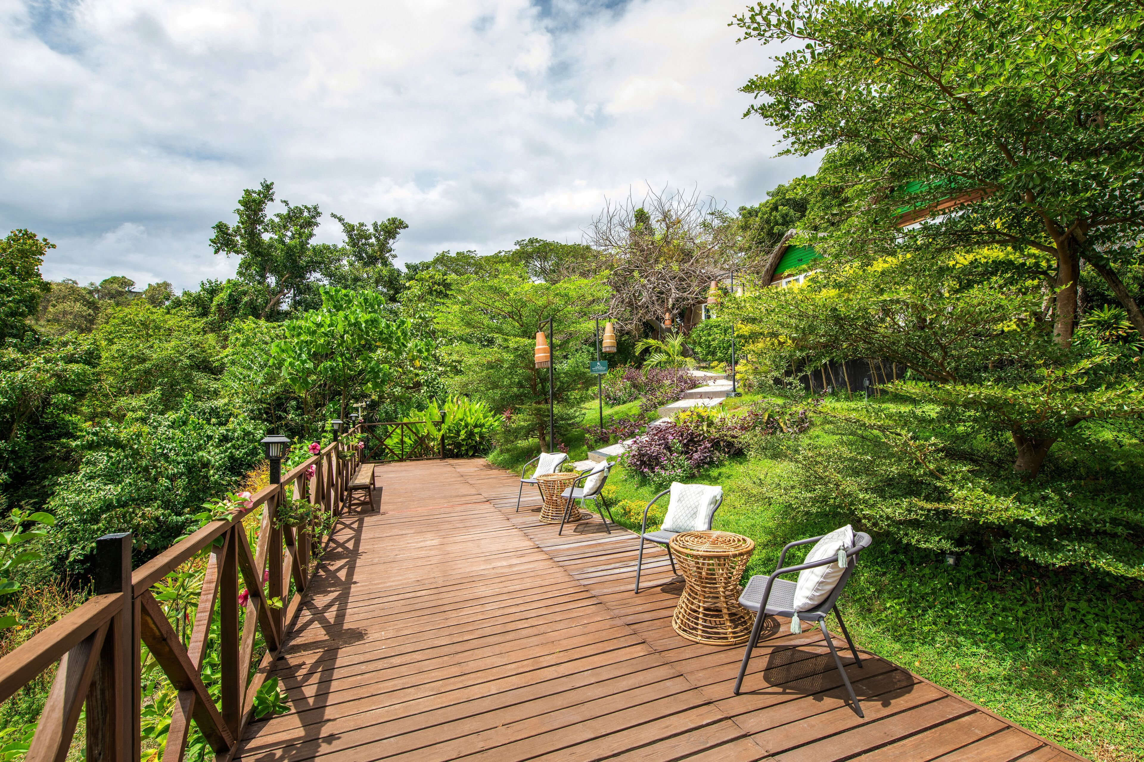 Une terrasse en bois avec des chaises en osier et un sentier qui traverse un jardin luxuriant.