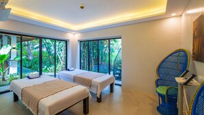 Une chambre avec deux lits, de grandes fenêtres, un fauteuil bleu et un luminaire au plafond.