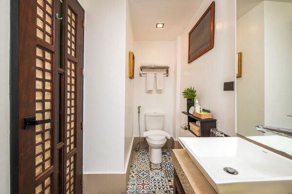 A bathroom with a toilet, a sink, a shower, a patterned floor, and a wooden door.