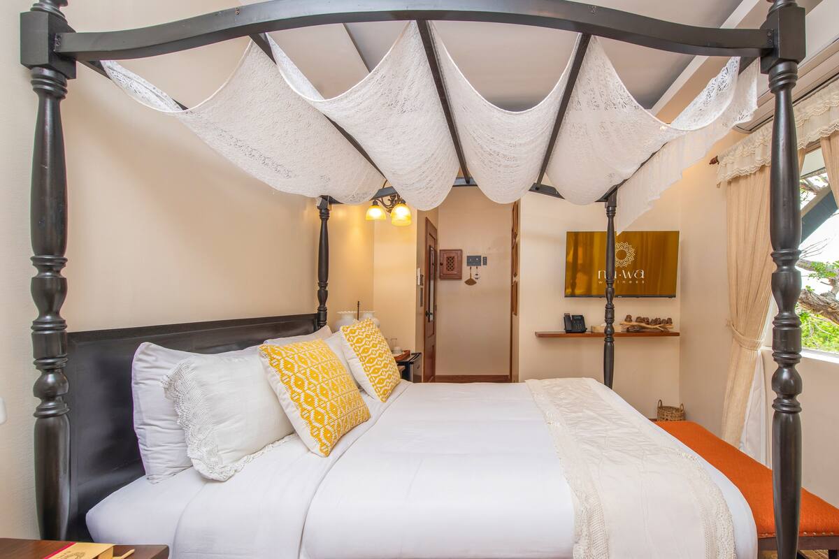 A four-poster bed with a canopy, a bedside table, a nightstand, and a mirror on the wall.