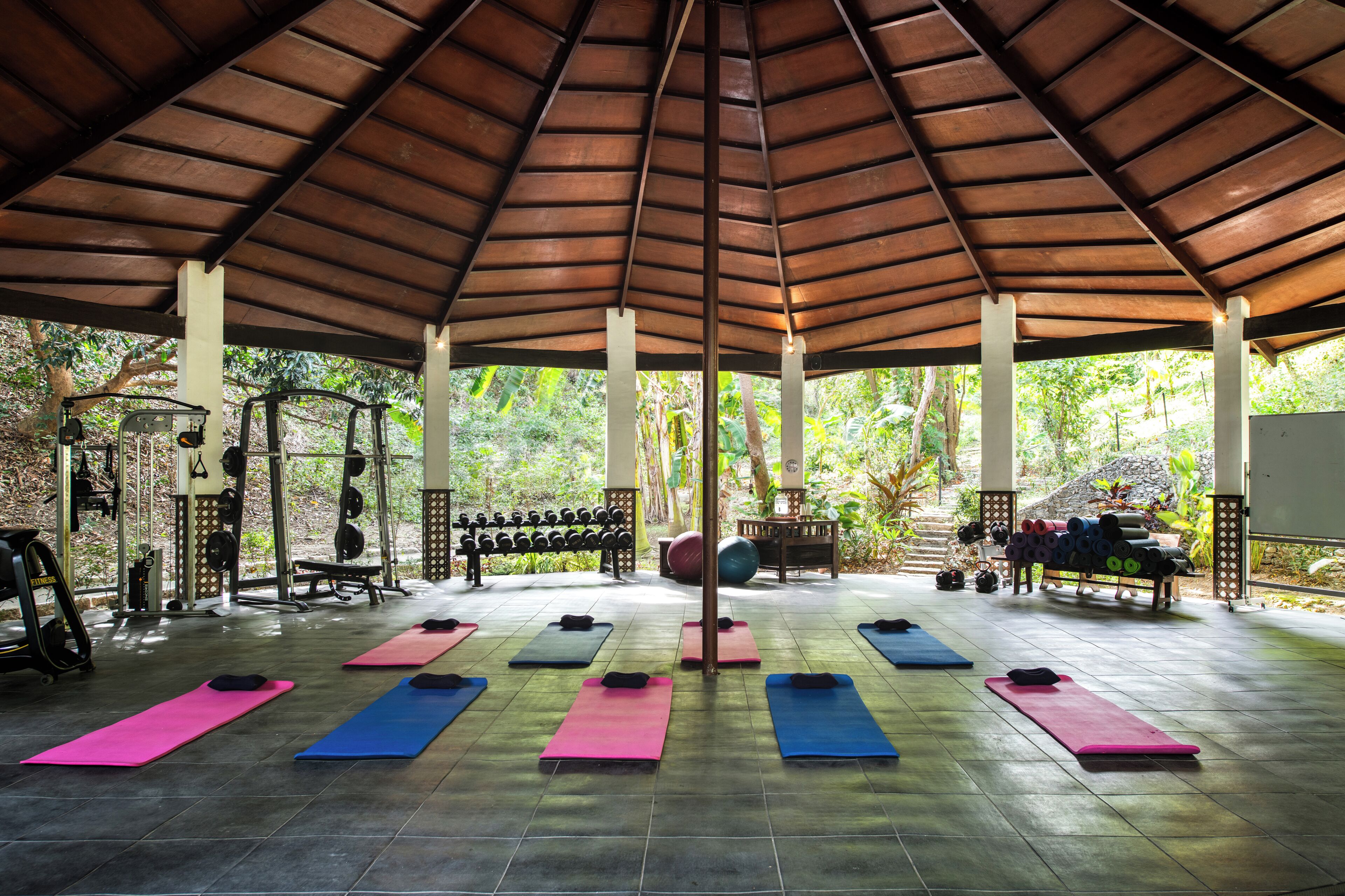 A covered gym area with exercise mats, weights, and a squat rack.
