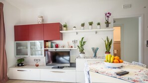 A modern kitchen with a red cabinet, white countertops, and a dining area with a floral tablecloth. - Apartment 50 meters from the sea in Taormina, with free private parking (Mazzeo)