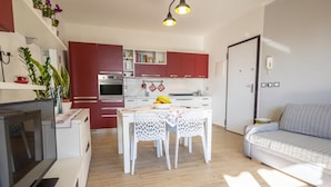 A modern kitchen with red cabinets, a dining table with a white lace tablecloth, and a grey sofa in a bright living area. - Apartment 50 meters from the sea in Taormina, with free private parking (Mazzeo)