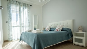 A bedroom with a bed, a nightstand, a mirror, and a window with curtains. - Apartment 50 meters from the sea in Taormina, with free private parking (Mazzeo)