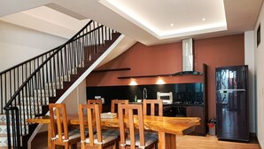 Une cuisine moderne avec une table et des chaises de salle à manger en bois, un réfrigérateur noir et un escalier avec des rampes noires.