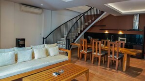 Un salon moderne comprenant un canapé, une table basse et un coin repas avec des chaises. Un escalier mène à un niveau supérieur.