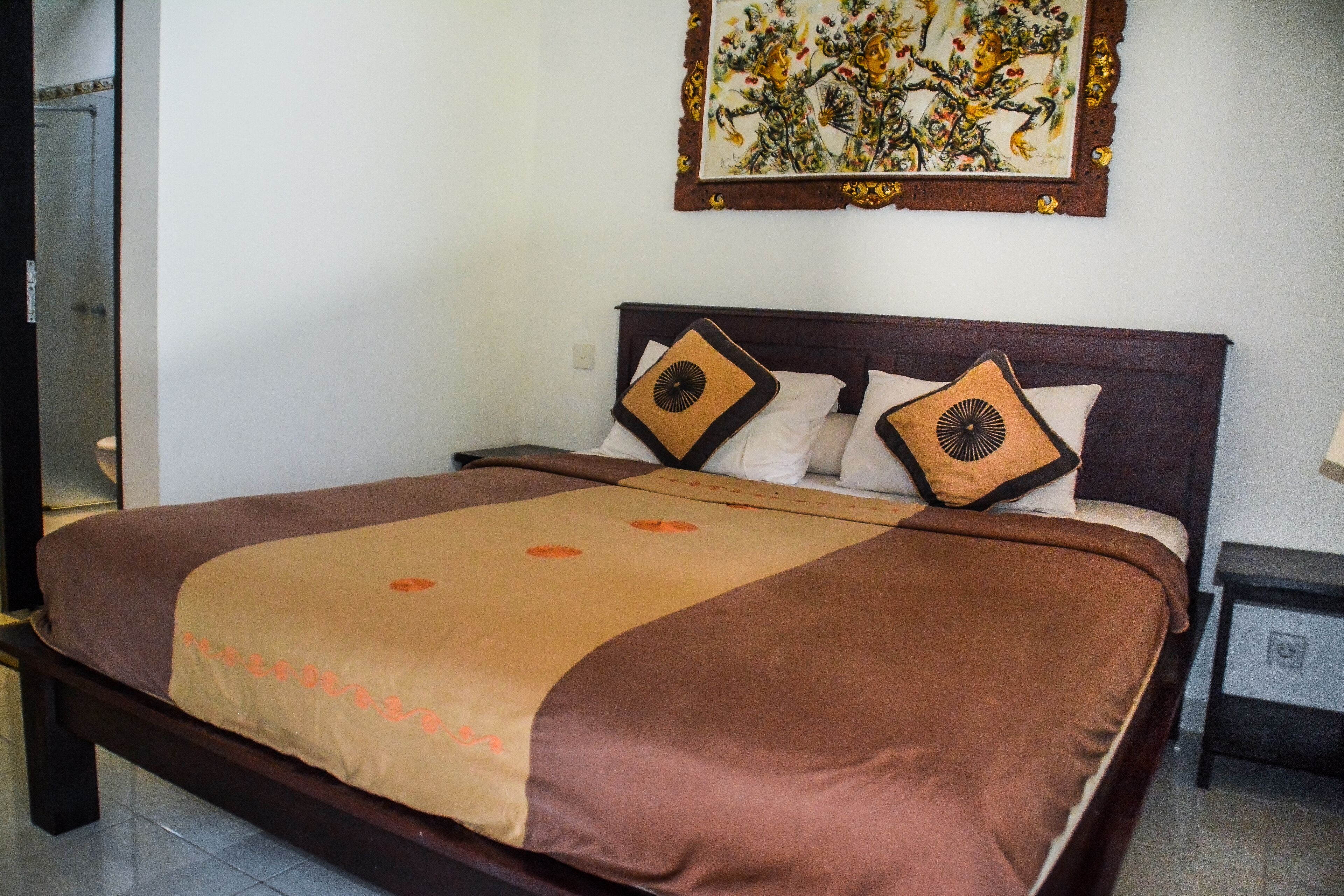 A neatly made bed with a brown and beige bedspread, two decorative pillows, and a framed artwork above the bed.