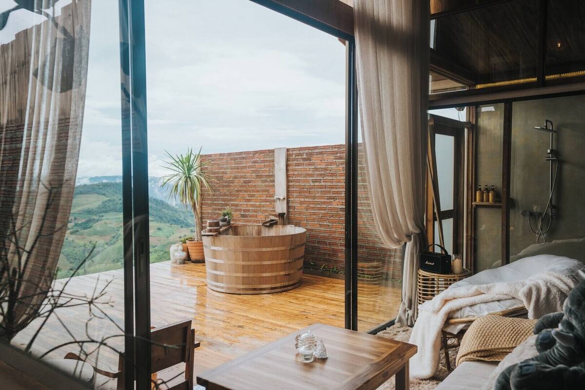 A modern room with a large wooden bathtub, a bed, and a table with a decorative item.