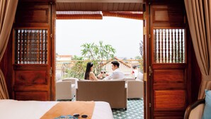 A hotel room with a bed, a dining table with two chairs, and a balcony with a view of the sky and a tree. - 75 Garden INN (Hue)