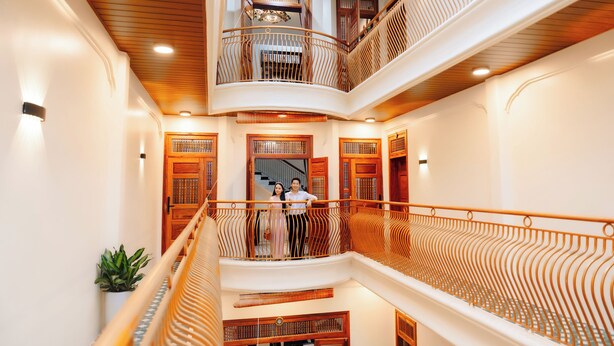 A multi-level interior with wooden railings, a staircase, and a view of a couple on the upper level. - 75 Garden INN (Hue)