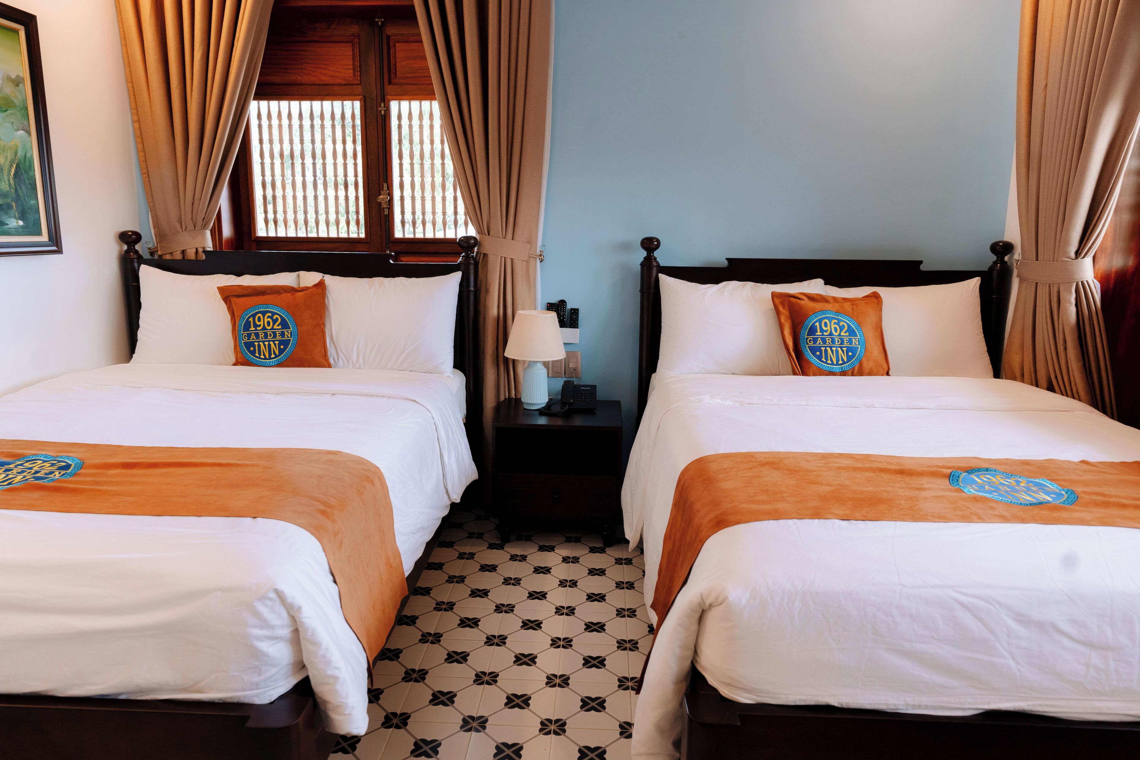 A hotel room with two beds, beige curtains, and a patterned floor.