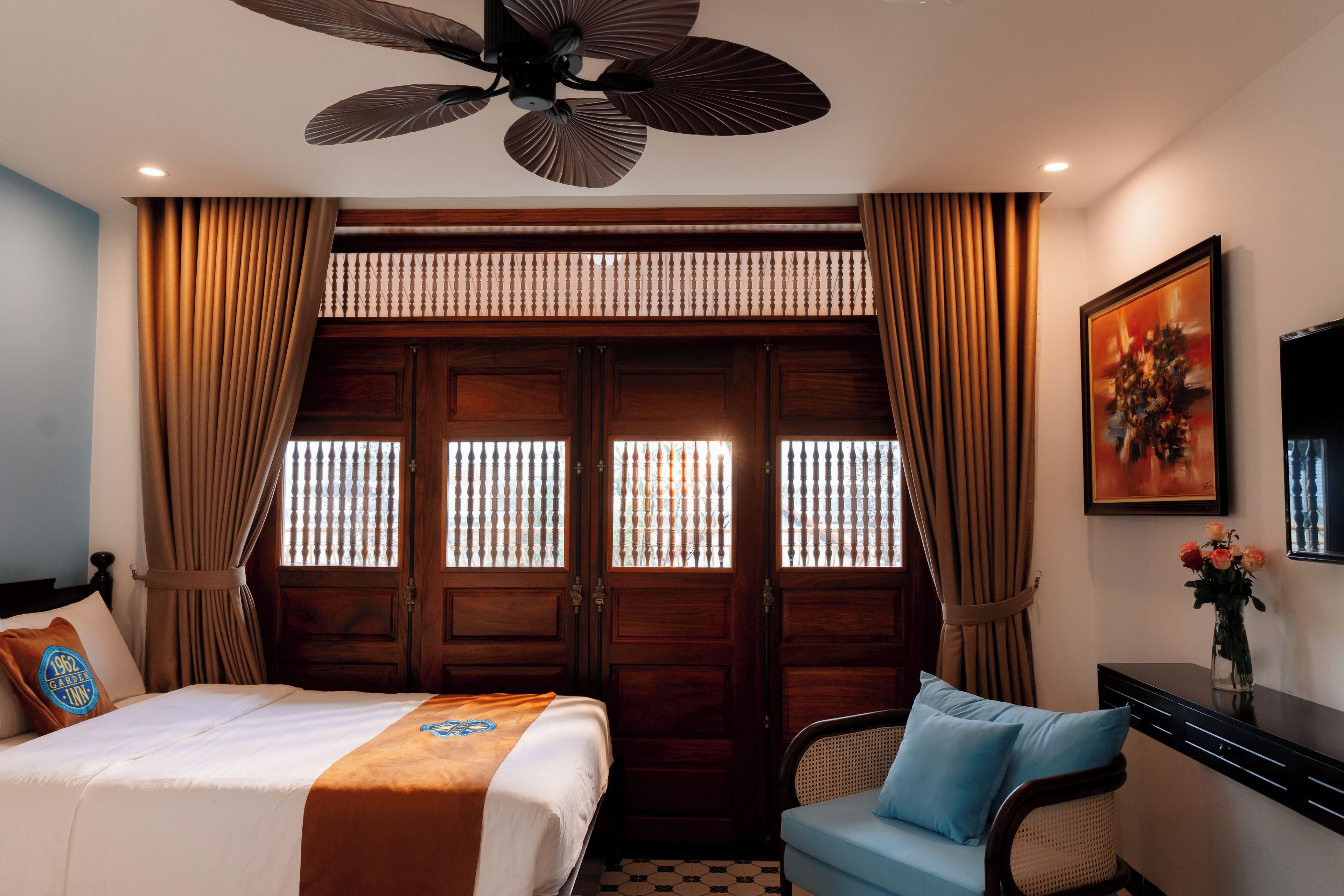 A hotel room with a bed, a desk, a chair, a ceiling fan, and a window with curtains.