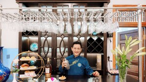 A bar area with a bartender holding a bottle, a tray with pastries, and a wine rack with glasses. - 75 Garden INN (Hue)