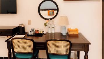 A hotel room with a dining table, two chairs, a mirror, a painting, a television, and an air conditioner.