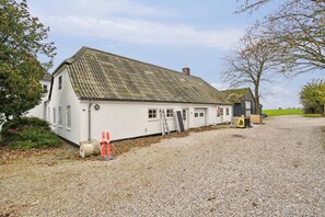 A white building with a sloped roof, a gravel driveway, and a small garden area.