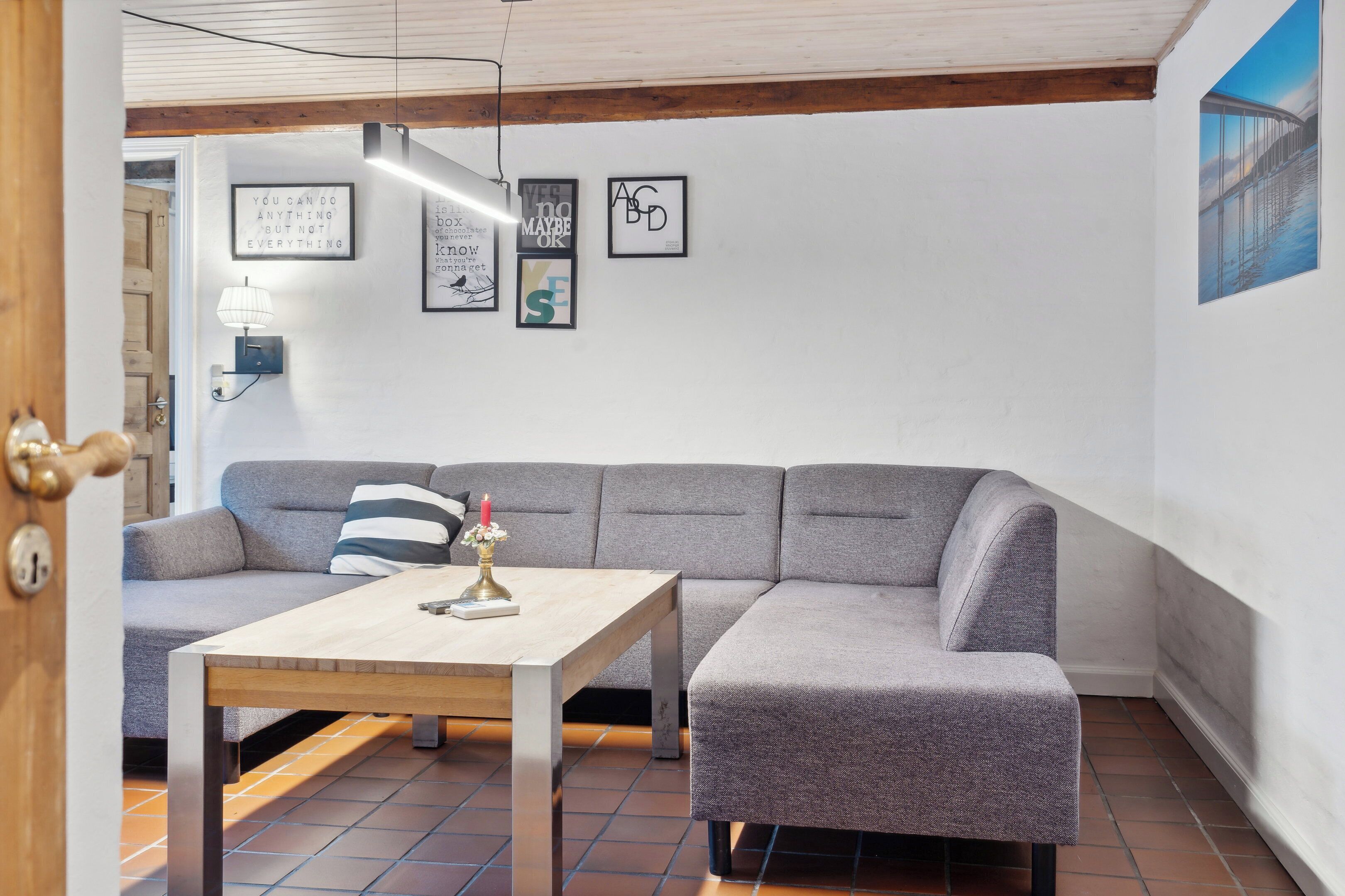 Un salon moderne avec un canapé gris, une table basse en bois et un mur orné de citations inspirantes encadrées.