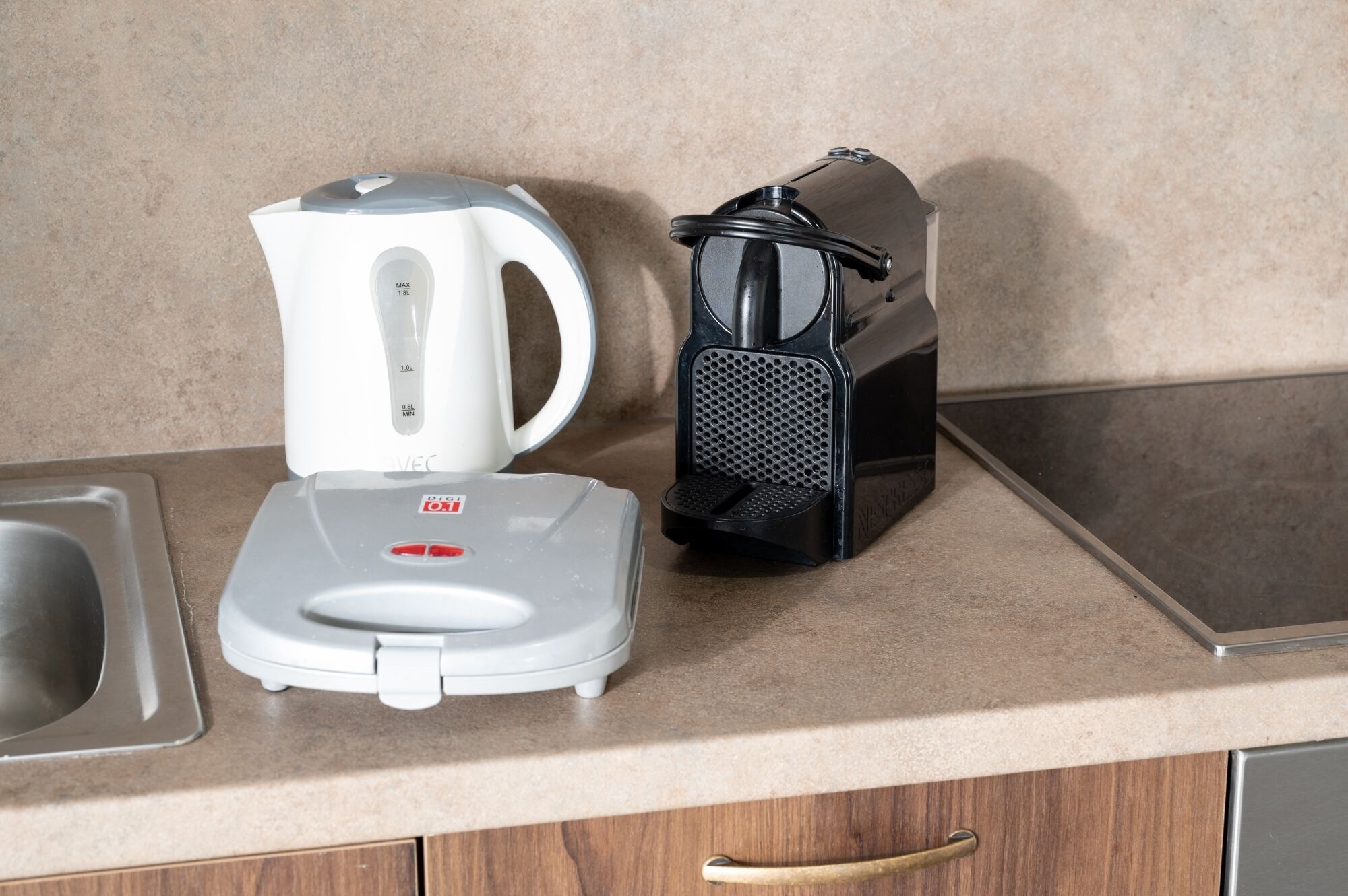A kitchen counter with a white electric kettle, a black coffee maker, and a stainless steel sink.