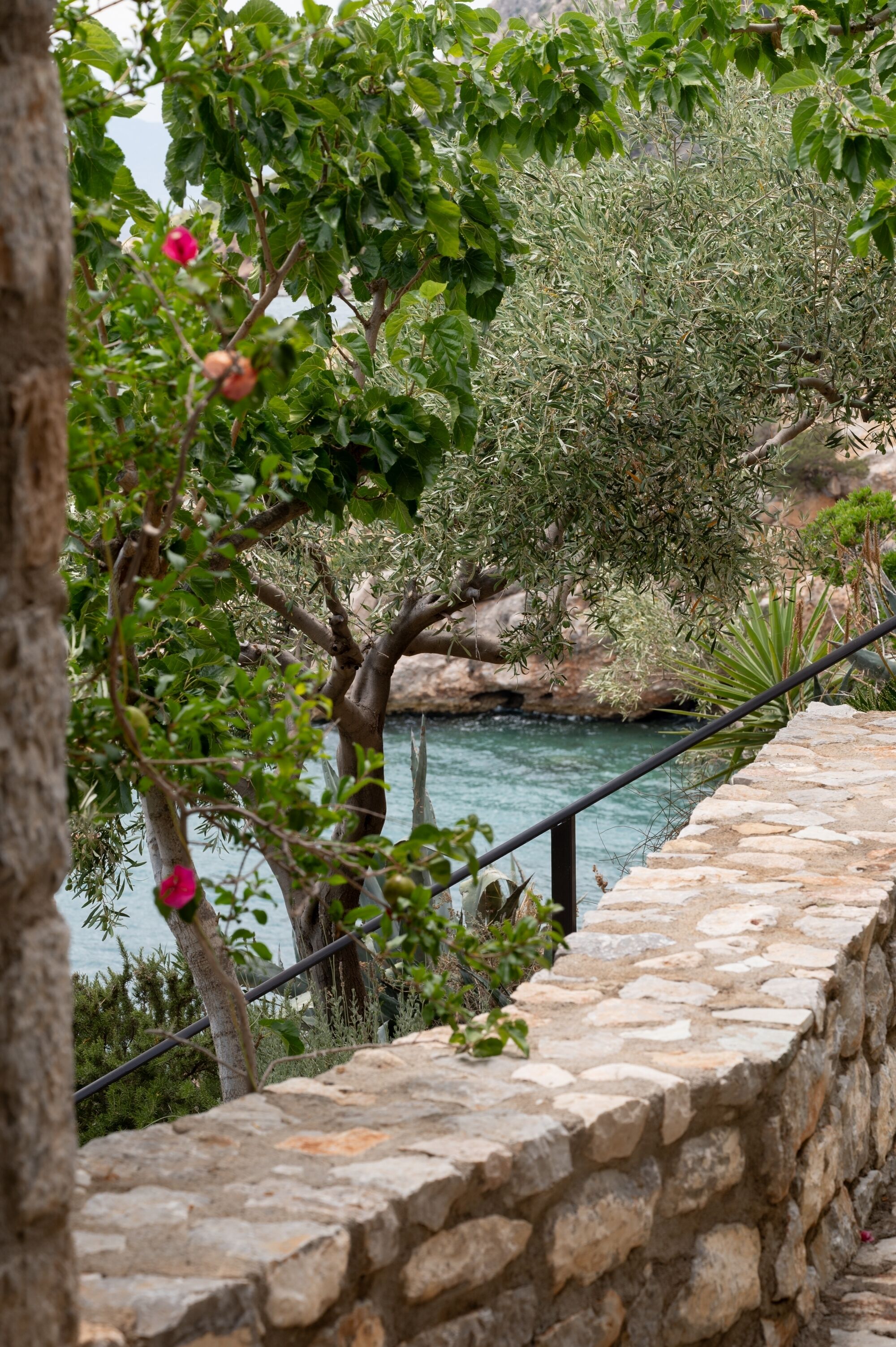 A stone wall with a railing overlooking a body of water and greenery.