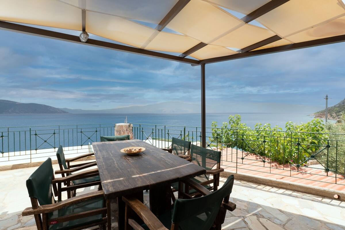 An outdoor patio with a table and chairs, overlooking a body of water and hills.