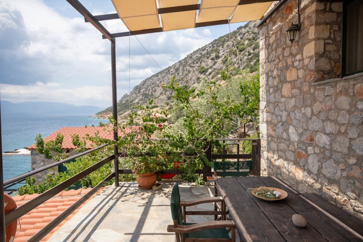 A balcony with a view of the sea, a table with a plate of food, and potted plants.