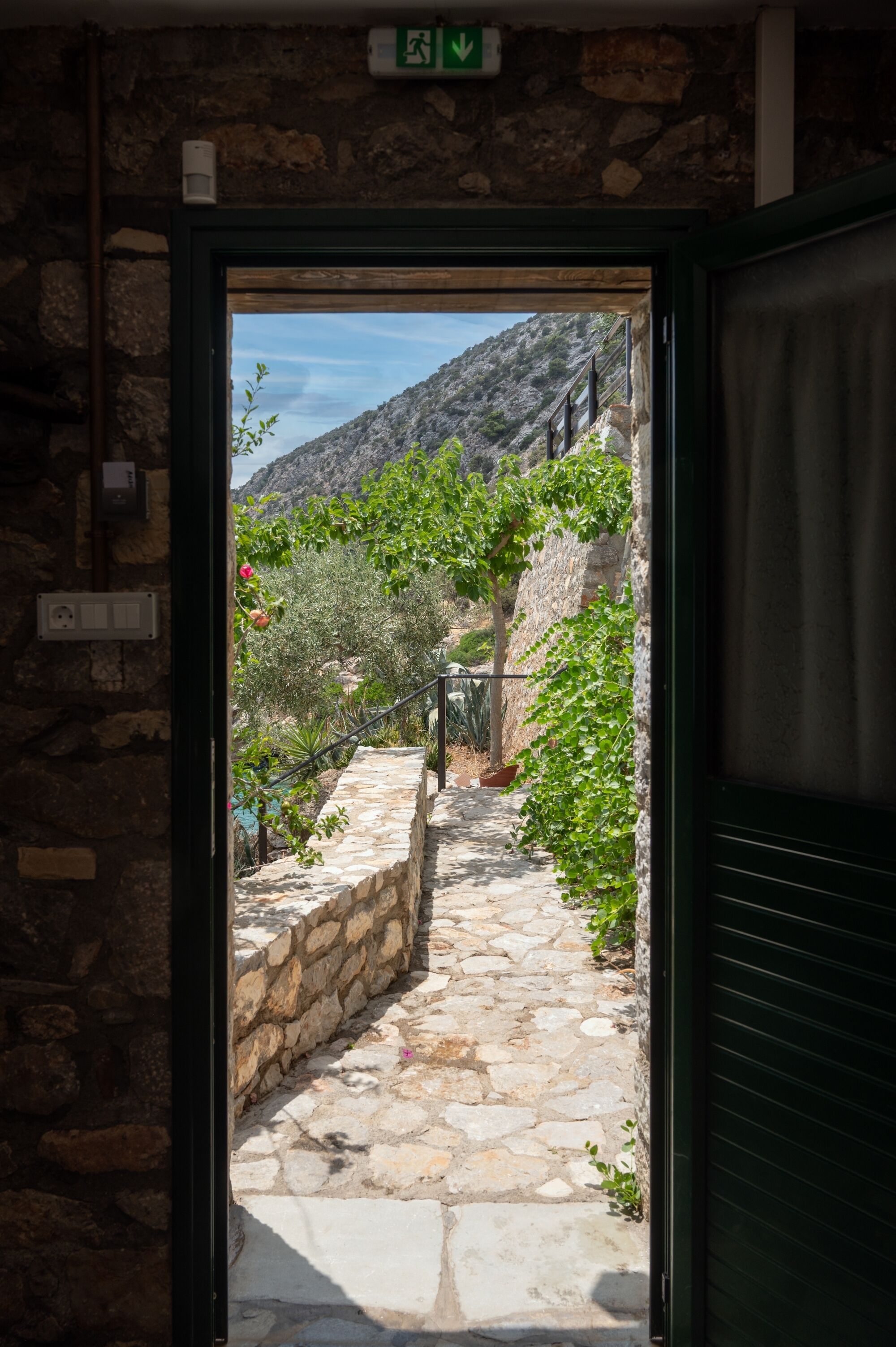 A stone pathway leading to a mountainous landscape with a stone wall and greenery.