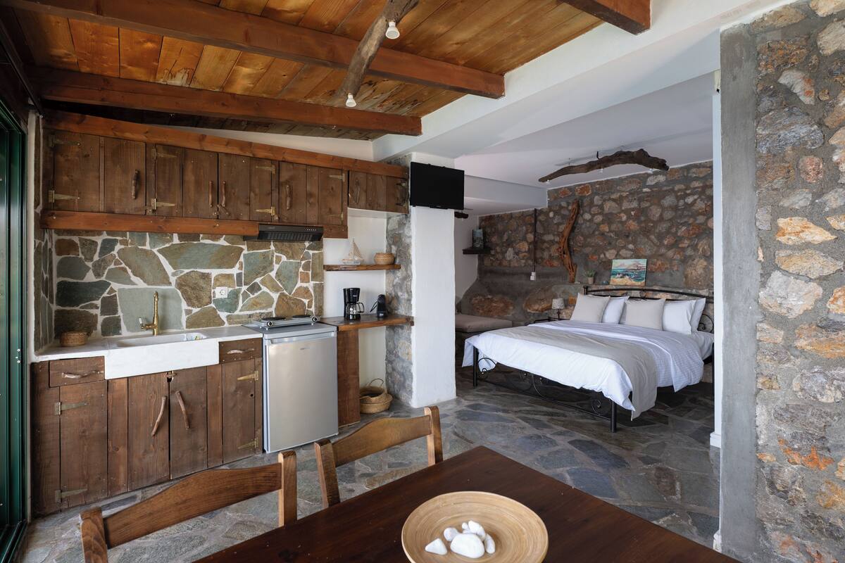 A rustic room with a stone wall, wooden cabinets, a bed, and a small kitchenette.