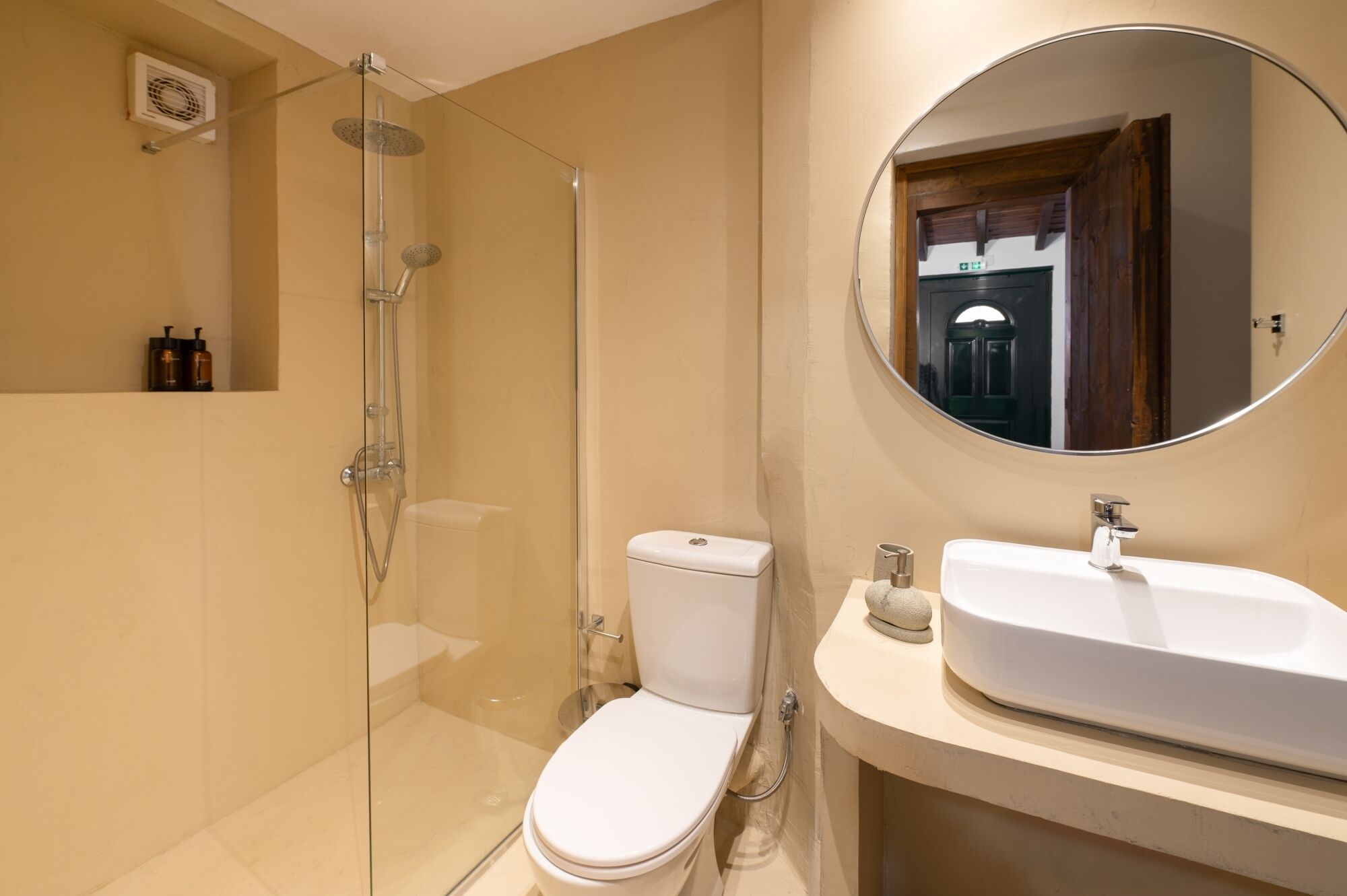 A modern bathroom with a glass-enclosed shower, a white toilet, and a round mirror above a white sink.