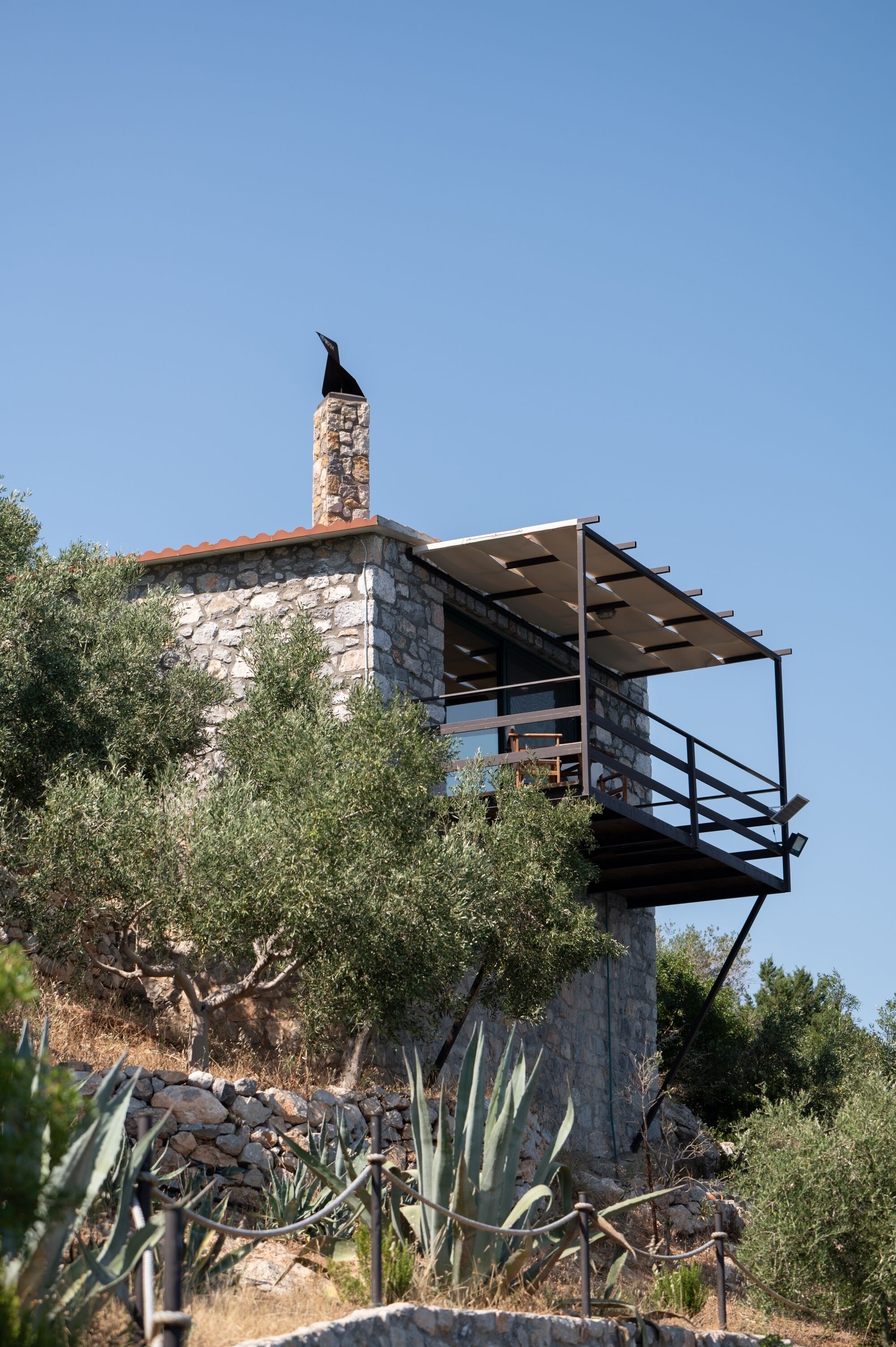 A stone building with a metal balcony, surrounded by vegetation.