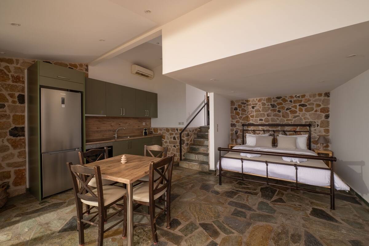 A compact kitchen with a built-in refrigerator, a dining table with chairs, and a stone wall.