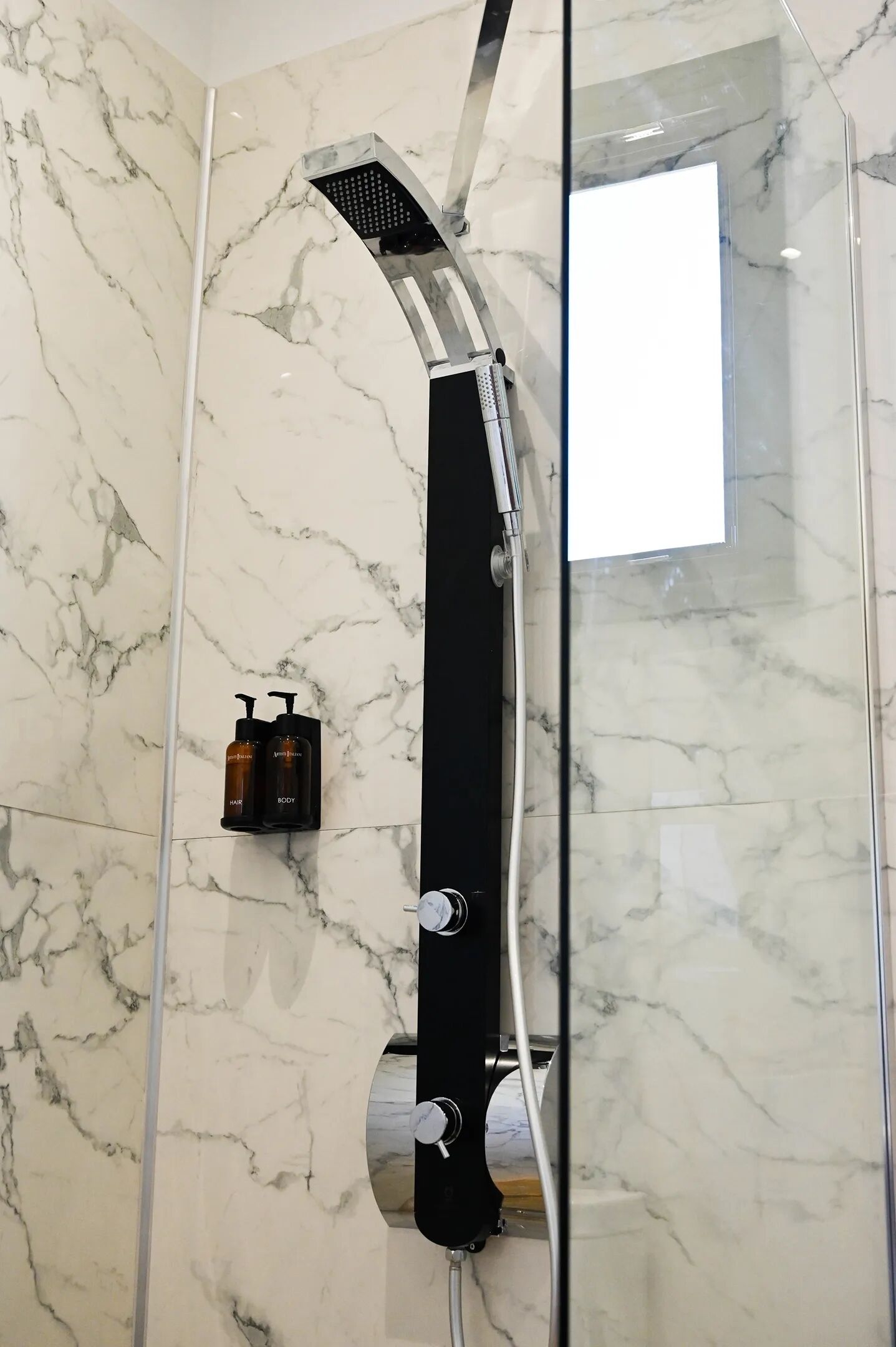 A shower with a curved head, a glass enclosure, and two bottles of shampoo on the wall.