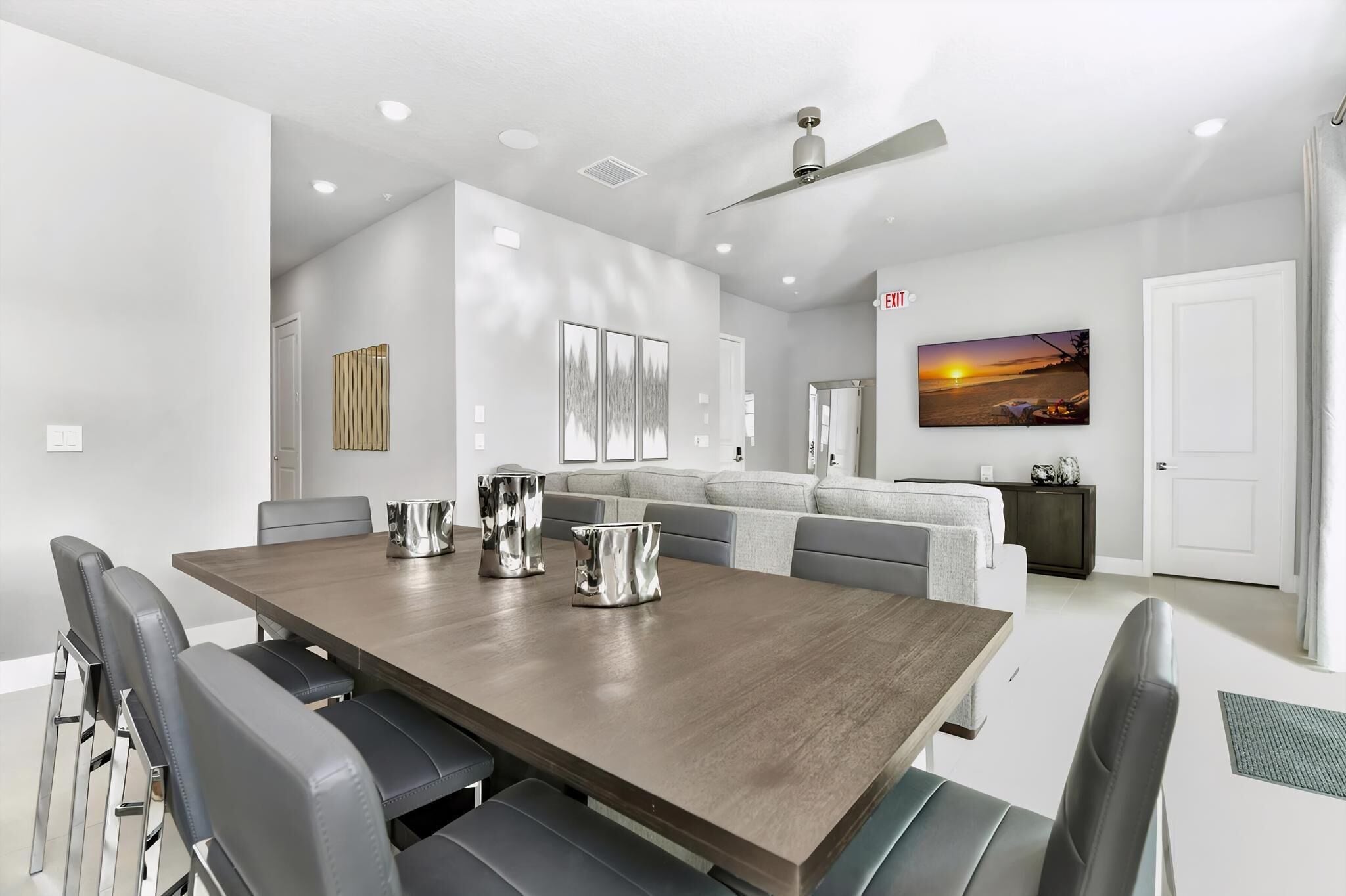 A modern dining area with a long table, black chairs, and a ceiling fan.
