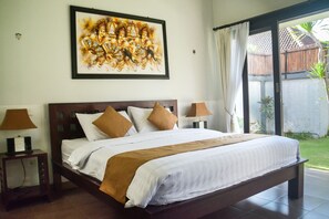 A large bed with a wooden headboard, white bedding, and brown pillows. There is a framed artwork above the bed and two bedside tables with lamps.