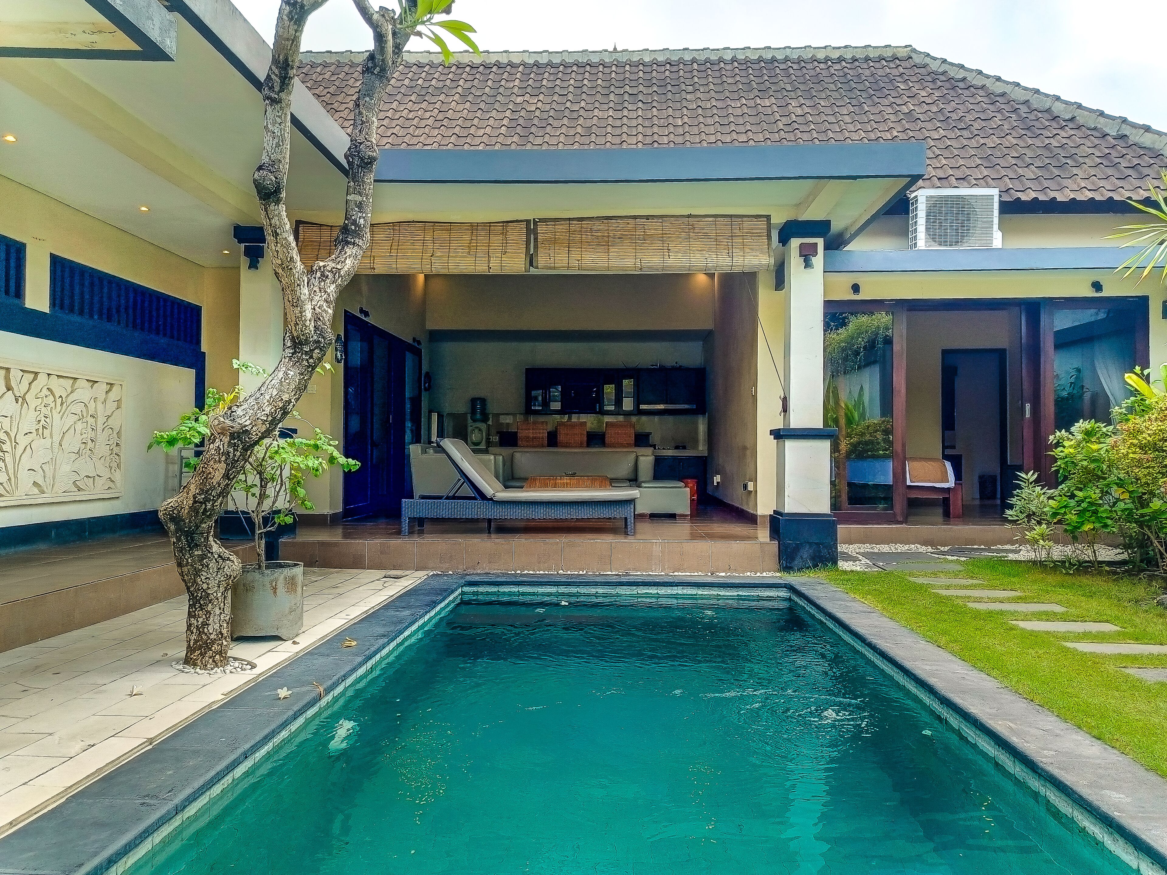 A swimming pool with a covered patio area, a kitchen with a TV, and a dining area.