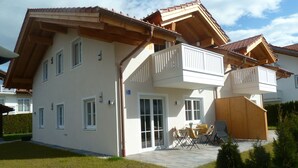 A two-story house with a balcony, a patio with outdoor furniture, and a well-maintained lawn. - Ferienwohnung Seeblick, 1-4 Pers., 1 Sep. Schlafzimmer, Südbalkon (Chieming)
