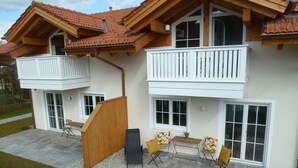 A two-story house with a balcony, a patio with seating, and a small garden area. - Ferienwohnung Seeblick, 1-4 Pers., 1 Sep. Schlafzimmer, Südbalkon (Chieming)