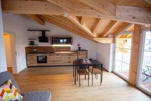 A modern kitchen with wooden beams, a dining area with a table and chairs, and a large window providing natural light. - Ferienwohnung Bergblick, 1-4pers., 1sep. Schlafzimmer, Südbalkon (Chieming)