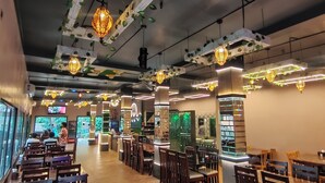A restaurant with wooden tables and chairs, decorative hanging lights, and a modern ceiling design.
