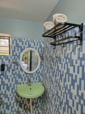 A bathroom with a patterned tile wall, a green sink, a round mirror, and a towel rack with two towels.