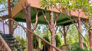A wooden staircase with metal railings leading to a balcony with a view of greenery.