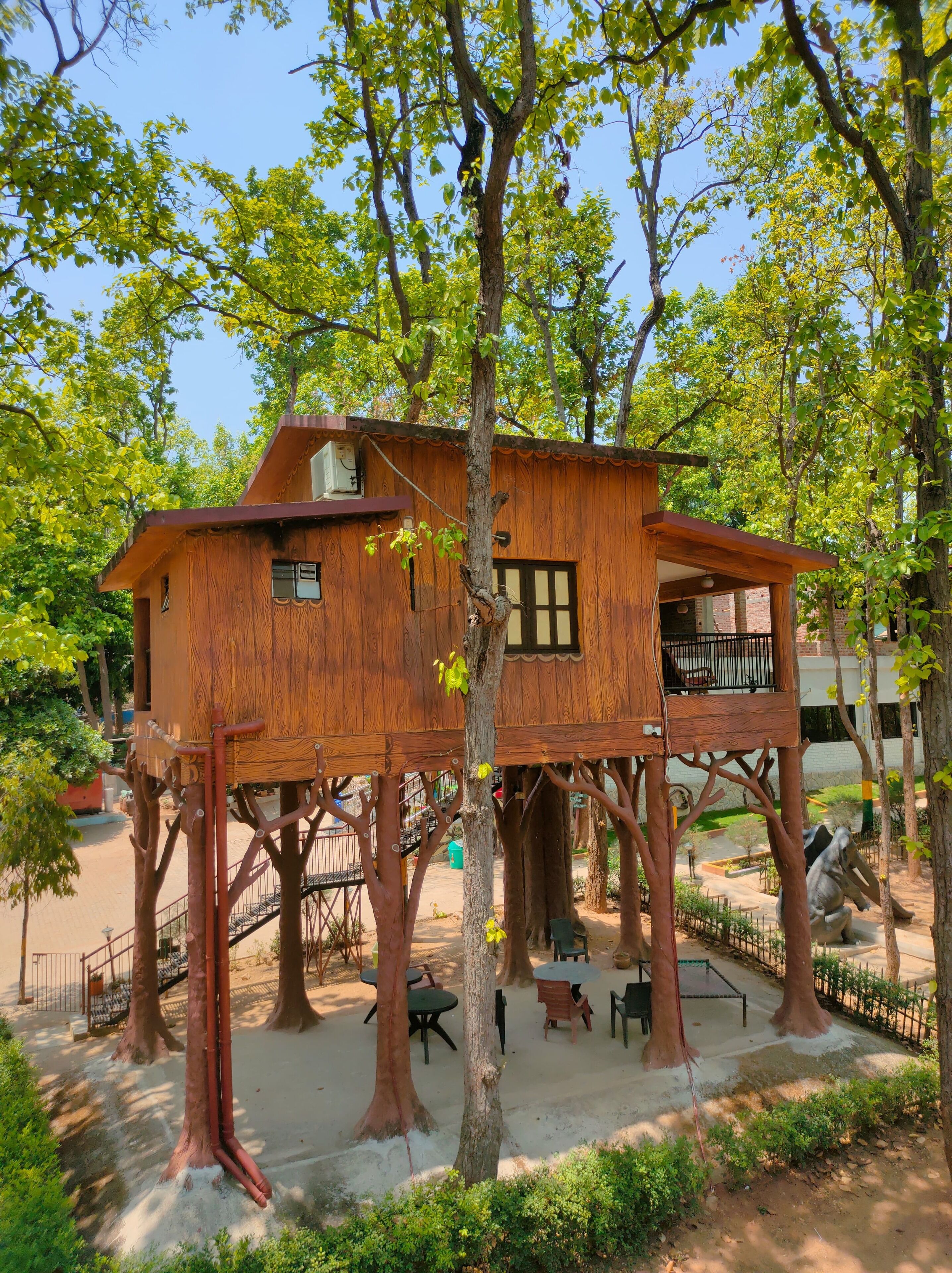 A treehouse with a wooden exterior, built on stilts, surrounded by trees and greenery.
