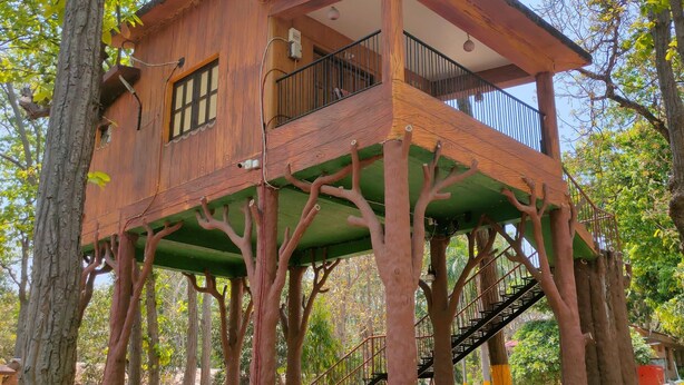 A treehouse with a balcony, surrounded by trees and a small outdoor seating area.