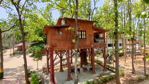 A wooden treehouse structure elevated among trees, with a balcony and a small window.
