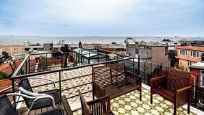 A rooftop terrace with a view of the sea, featuring a tiled floor, wooden benches, and a glass balustrade. - Room-deluxe Double Room 4 (Istanbul)
