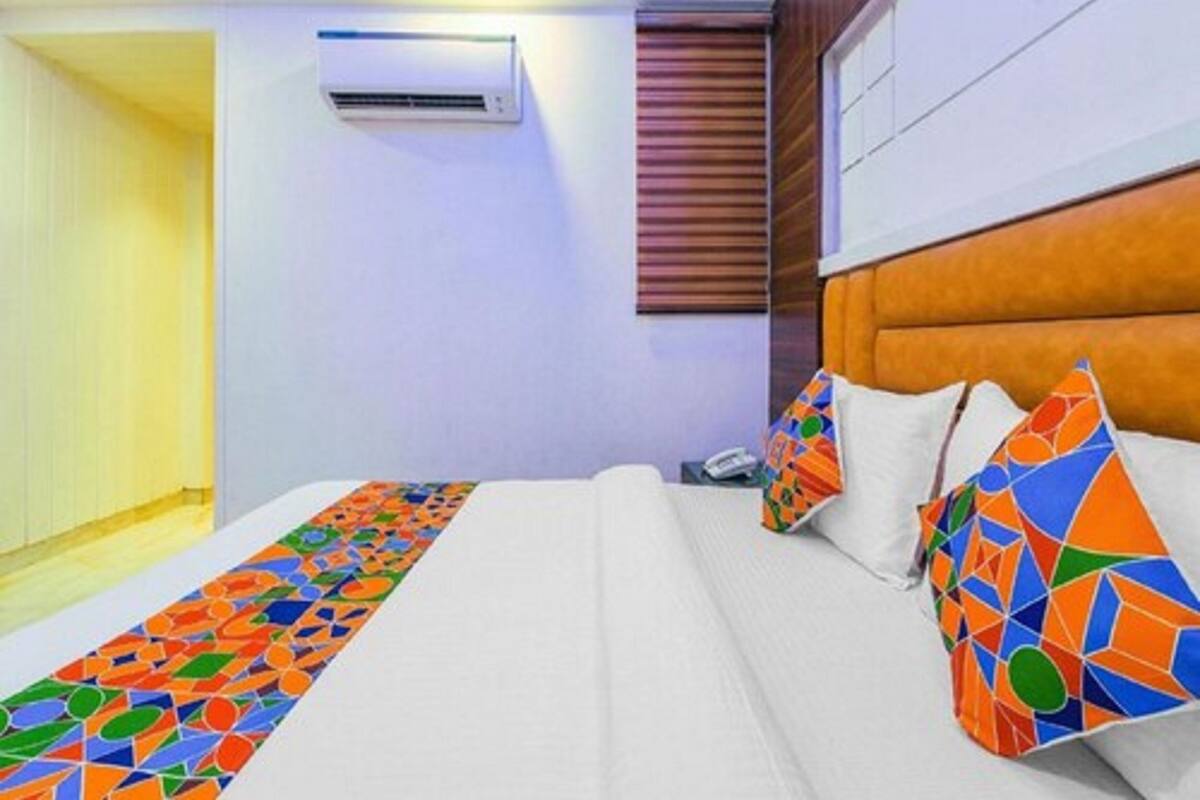 A hotel room with a bed, a colorful runner, a headboard, and an air conditioning unit on the wall.