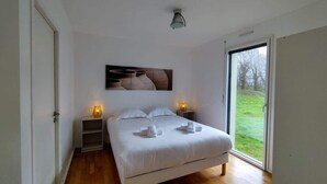 A bedroom with a bed, bedside lamps, a large window, and a view of the outdoors.