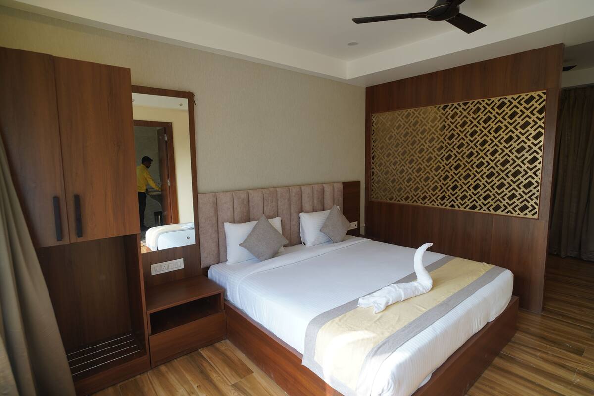 A neatly arranged bedroom with a large bed, wooden wardrobe, and a mirror.