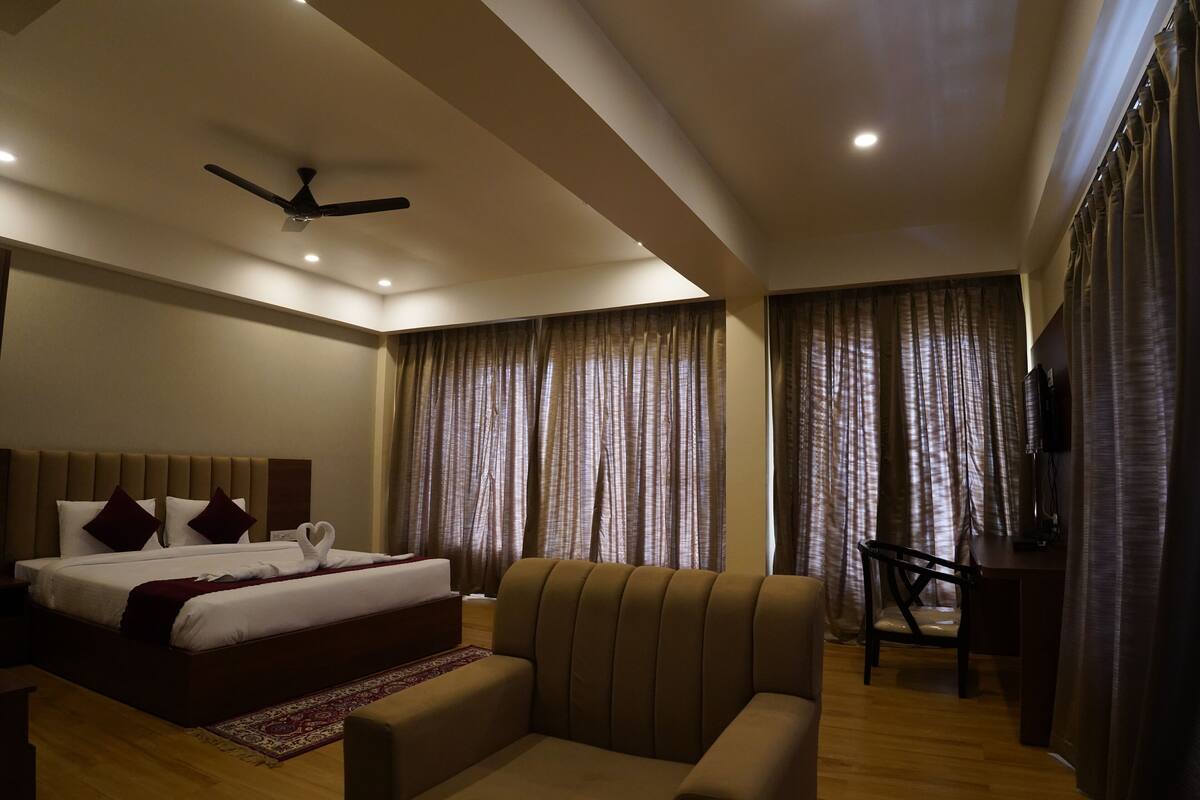 A hotel room with a bed, a sofa, a desk, curtains, and a ceiling fan.