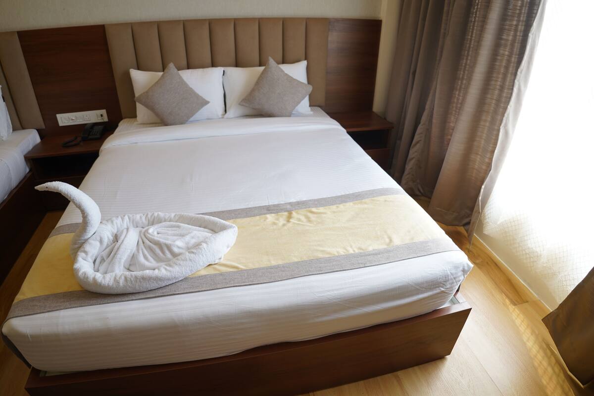 A hotel room with a large bed, a bedside table with a phone, and a window with curtains.