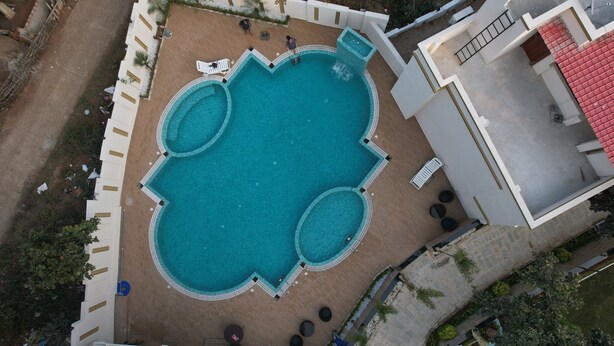 Eine Vogelperspektive auf ein Hotel mit einem zentralen Schwimmbad, mehreren Liegebereichen und einer überdachten Terrasse.