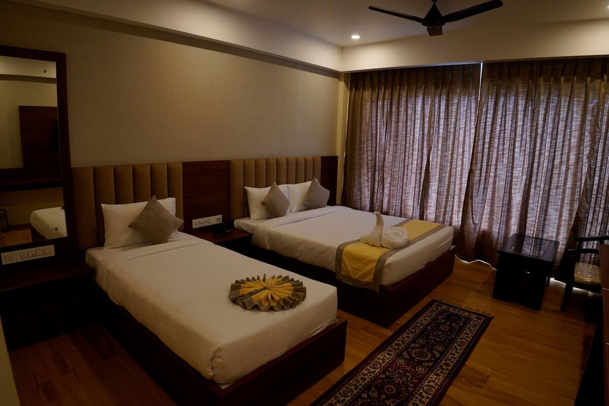 A hotel room with two beds, a ceiling fan, a large mirror, a nightstand, a bedside table, and a window with curtains.